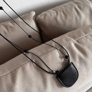 Minimalist black leather mini crescent pendant necklace bag on beige fabric background