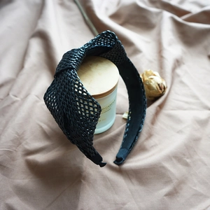 Close-up of black raffia woven headband featuring intricate mesh texture on a cozy fabric