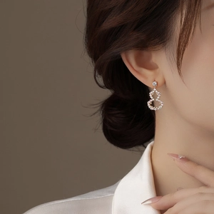 Close-up of elegant gold gourd-shaped earrings with pink and white inlaid diamonds on a model