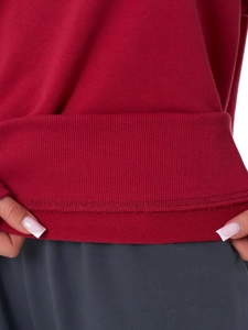 Detailed close-up of the ribbed hem and double-stitched seams on the red cotton sweatshirt