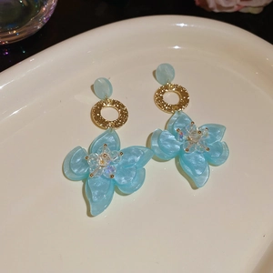 Detailansicht hellblauer Harzblumenohrringe mit goldenen Ringen und Kristallzentrum