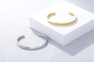 Close-up of gold and silver C-shaped bracelets with One Life One Love engraving