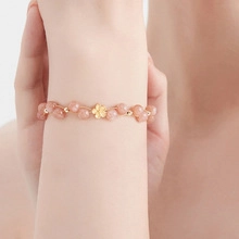 Close-up of beaded stone bracelet with golden floral charm on a person's wrist