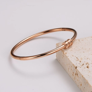 Elegant rose gold stainless steel bangle with diamond accents on a textured stone base