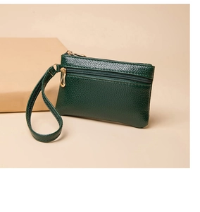 Close-up of green pebble grain leather coin purse with double gold zippers and wrist strap