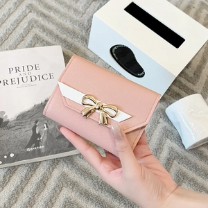Detail of pink faux leather wallet featuring a contrast white flap and gold bow metal clasp