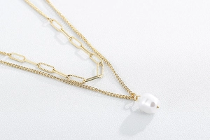 Detail of layered gold paperclip chain necklace with a white baroque pearl pendant