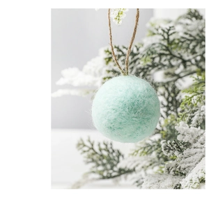 Close-up of mint green wool felt ball ornament hanging on snowy pine branch