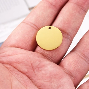 Close-up of a polished gold stainless steel round charm pendant held in a person's hand