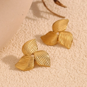 Macro shot of 18K gold plated petal earrings with vertical texture on a sandy surface