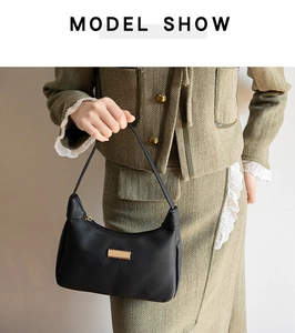 Close-up of black lychee leather underarm bag with gold metal buckle on green blazer