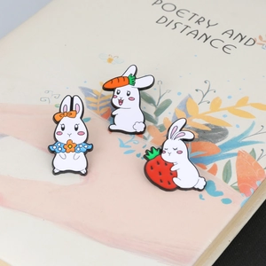 Detailed view of white enamel rabbit pins with carrots and strawberries on a book