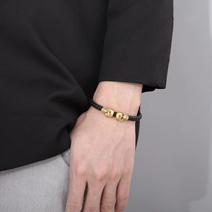 Close-up of a braided leather bracelet featuring two golden skull accents on a wrist