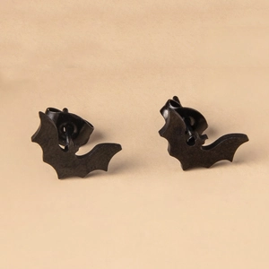 Macro shot of matte black bat stud earrings for Halloween on light brown background