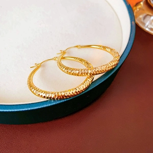 Vue macro de boucles d'oreilles créoles dorées texturées sur un plateau à bijoux vert