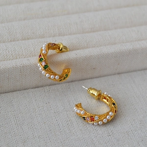 Macro shot of gold-plated C-shaped twisted earrings with pearls and colorful zircons