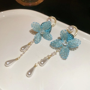 Detail of blue mesh flower earrings with pearls on a white ceramic plate