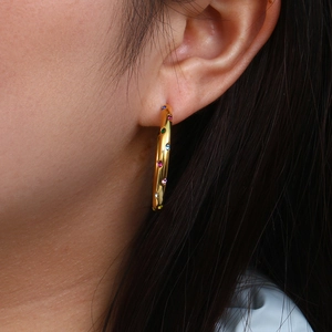 Detailed close-up of gold hoop earring with colorful rainbow zircons on model ear
