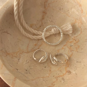 Macro view of textured silver rings and layered hoop earrings on marble surface