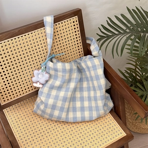 Detail of blue plaid canvas bag with floral charm on a vintage rattan chair background
