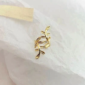 Macro view of 18k gold plated leaf branch ear cuff on elegant white textured paper