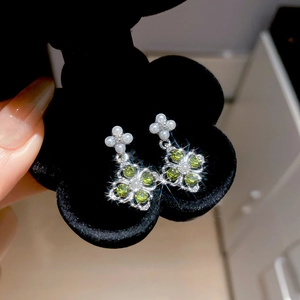 Detailed macro view of silver flower earrings with green stones and pearls on velvet box