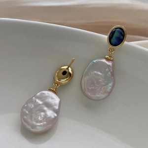 Detailed shot of baroque pearl earrings with blue gemstone and gold metal hardware