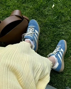 Vue détaillée de baskets en daim bleu à rayures blanches et sac en cuir marron sur l'herbe