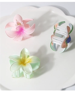 Detailed view of three pearlescent frangipani flower hair claws in pastel gradient colors