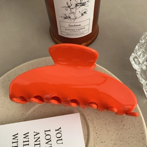 Detail of a glossy orange acetate hair claw clip displayed on a beige ceramic plate