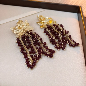 Detail of vintage gold leaf earrings with dark red grape bead tassels on a soft beige surface