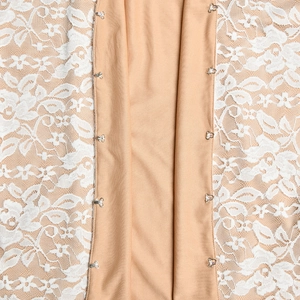 Détail macro du tissu en dentelle beige avec crochets métalliques sur un haut polo