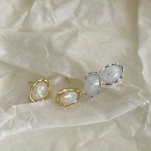 Macro shot of oval opal earrings with wavy gold and silver metal edges on soft paper