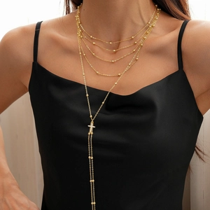 Detail of layered gold Y-necklace with beaded chains and sparkling cross pendant on model