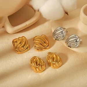 Detailed view of geometric textured 18K gold and silver stud earrings on a beige fabric