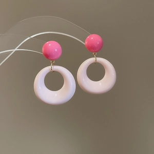 Close-up of pink resin drop earrings featuring circular asymmetrical design on a clear stand