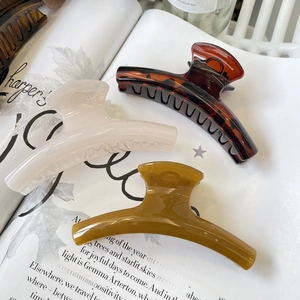 Three elegant French hair claw clips in beige, tortoiseshell and amber on a book