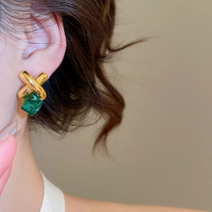 Detail view of gold cross stud earrings featuring a square emerald green gemstone