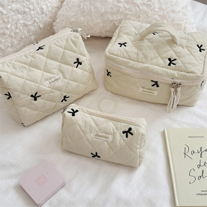 Three-piece beige quilted cosmetic bags set featuring elegant black bow embroidery