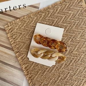 Close-up of resin chain hair clips in amber and marble white on a woven background