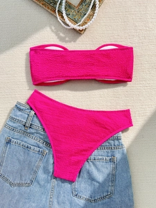 Flat lay of pink strapless bikini set with textured fabric on a stylish background