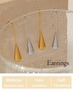 Detail view of gold and silver teardrop earrings in stainless steel on a glass rim