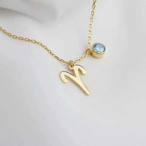 Gold Aries zodiac necklace with light blue gemstone pendant on a white fabric background