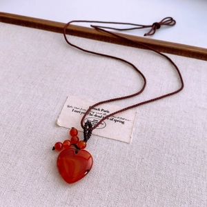 Macro detail of heart-shaped red agate pendant with brown braided cord on linen background