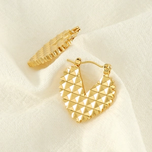 Detailed close-up of golden heart earrings with geometric pyramid texture on linen