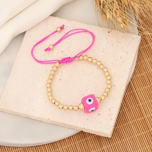 Pink evil eye woven bracelet with gold beads on a natural stone and wheat background