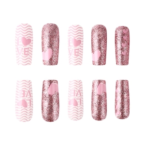 Detail of pink glossy press-on nails with heart patterns and glitter accents