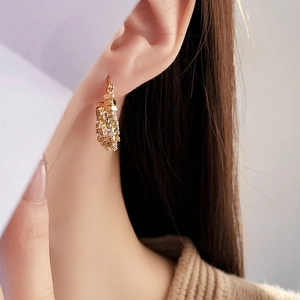 Detail of gold-plated U-shaped earrings with white zircon on a model's ear