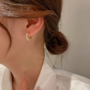 Close-up of elegant gold hoop earrings with white zircon stones worn on the earlobe