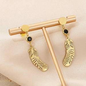 Détail de boucles d'oreilles plume dorées avec pierres noires sur un porte-bijoux